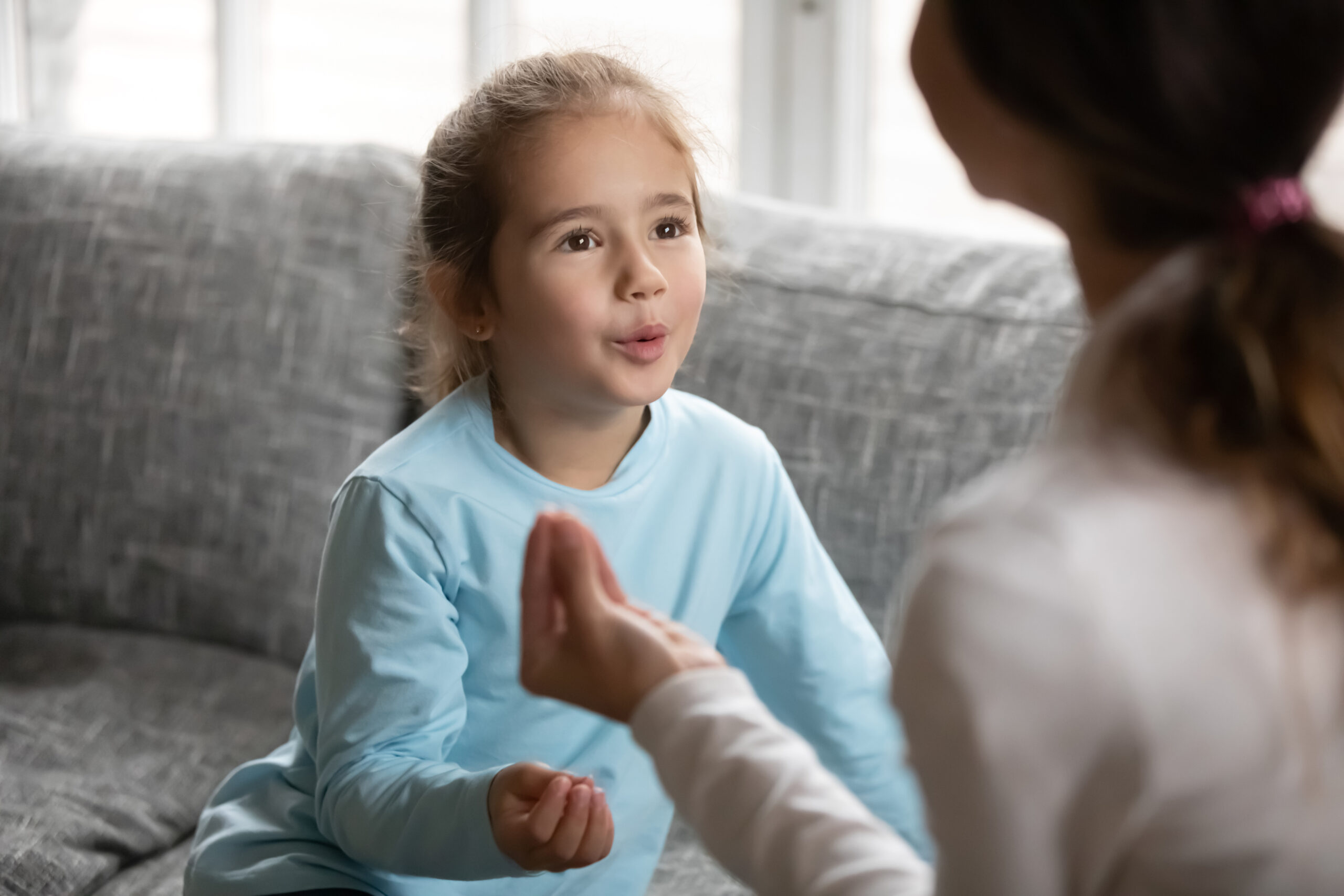 Adorable small focused 6s preschool disabled baby girl practicing correct sound pronunciation with speech therapist, making exercises at lesson, having problems or difficulties with speaking.